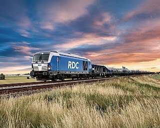 Der blaue AUTOZUG Sylt fährt vollbeladen in den Sonnenuntergang.