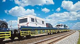 Ein Wohnwagen und ein Wohnmobil werden huckepack auf dem blauen AUTOZUG über den Sylt-Damm transportiert