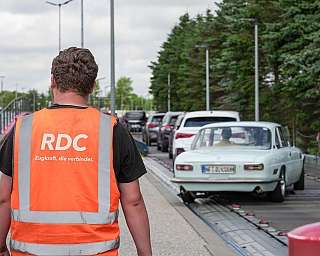 Es fahren PKW über die Laderampe auf den blauen AUTOZUG Sylt. Im Vordergrund steht ein Mitarbeiter mit dem Rücken zur Kamera.