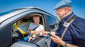 Mitarbeiter vom blauen AUTOZUG Sylt checkt Kunden im Fahrzeug ein.