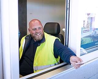 Ein Mitarbeiter vom blauen AUTOZUG Sylt reicht eine Fahrkarte aus dem Verkaufsfenster am Terminal.