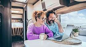 An older couple sits close together in front of a laptop in a motorhome.