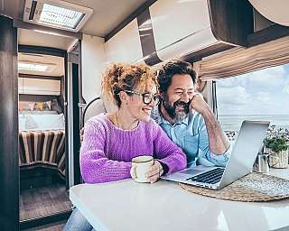 Ein älteres Ehepaar sitzt vertraut zusammen vor einem Laptop in einem Wohnmobil.