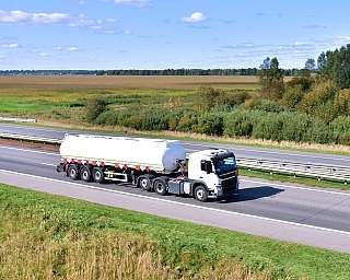 Ein LKW mit Gefahrtgut fährt auf einer Autobahn durch eine grüne Landschaft.