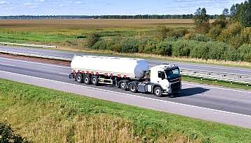 Ein LKW mit Gefahrtgut fährt auf einer Autobahn durch eine grüne Landschaft.
