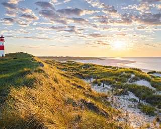 Blick über Dünen und Strand auf den Leuchtturm von List auf Sylt bei abendlicher Lichtstimmung.